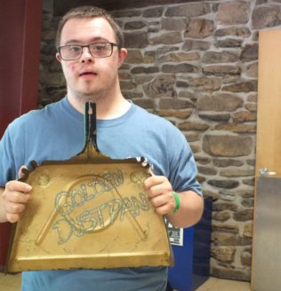 Kristie's son holds a dustpan with "Golden Dustpan" written on it.