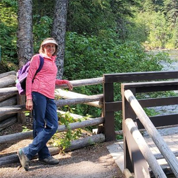 Carol poses for camera on a bridge over a river.