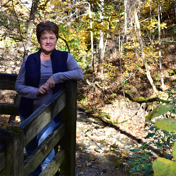 Peggy stands on a deck in the woods.