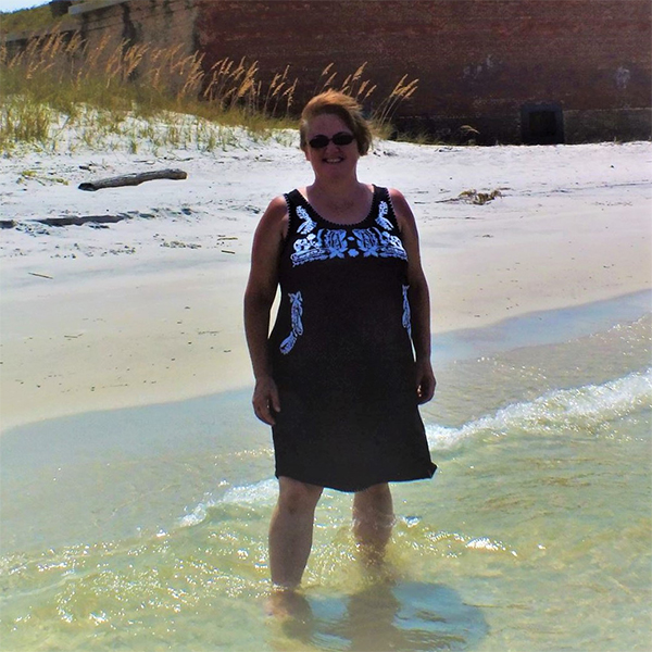 Peggy stands in the water on a sunny beach.