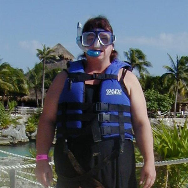 Vicky standing in front of palm trees wearing a snorkel and life vest.